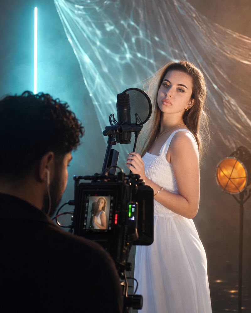 Musikvideo-Dreh im Studio: Sängerin am Mikrofon zwischen Neonlicht und Nebel, im Vordergrund der Kameramann am Monitor